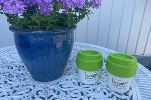 Bilde av kopper med Blidebarn logo sammen med bleblomst på hvitt smijernsbord.