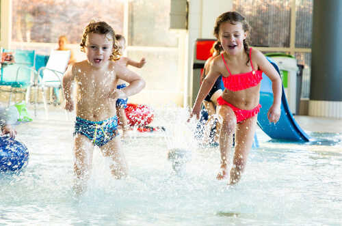 To glade barn som løper og spruter vann i basseng.