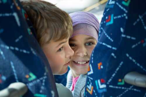 Bilde av to barn som ser i kamera mellom to blå buss-seter.
